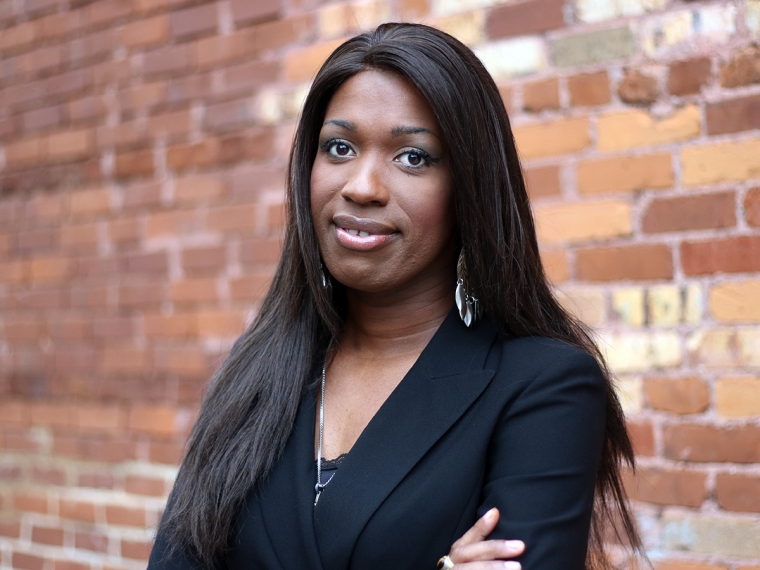 A young Black woman standing by a wall.